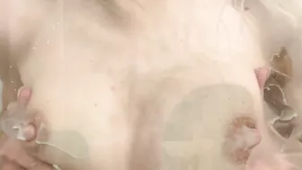 Sexy woman playfully splashes with her breasts in the shower while nursing her baby.