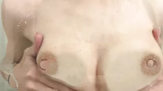 Sexy woman playfully splashes with her breasts in the shower while nursing her baby.